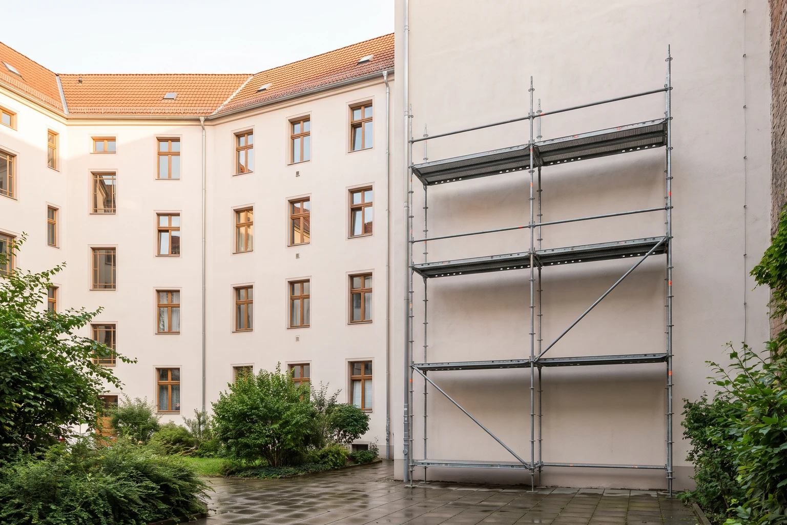 Mehrfamilienhaus mit einem Baugerüst an einem Teil der Fassade und begrüntem Innenhof